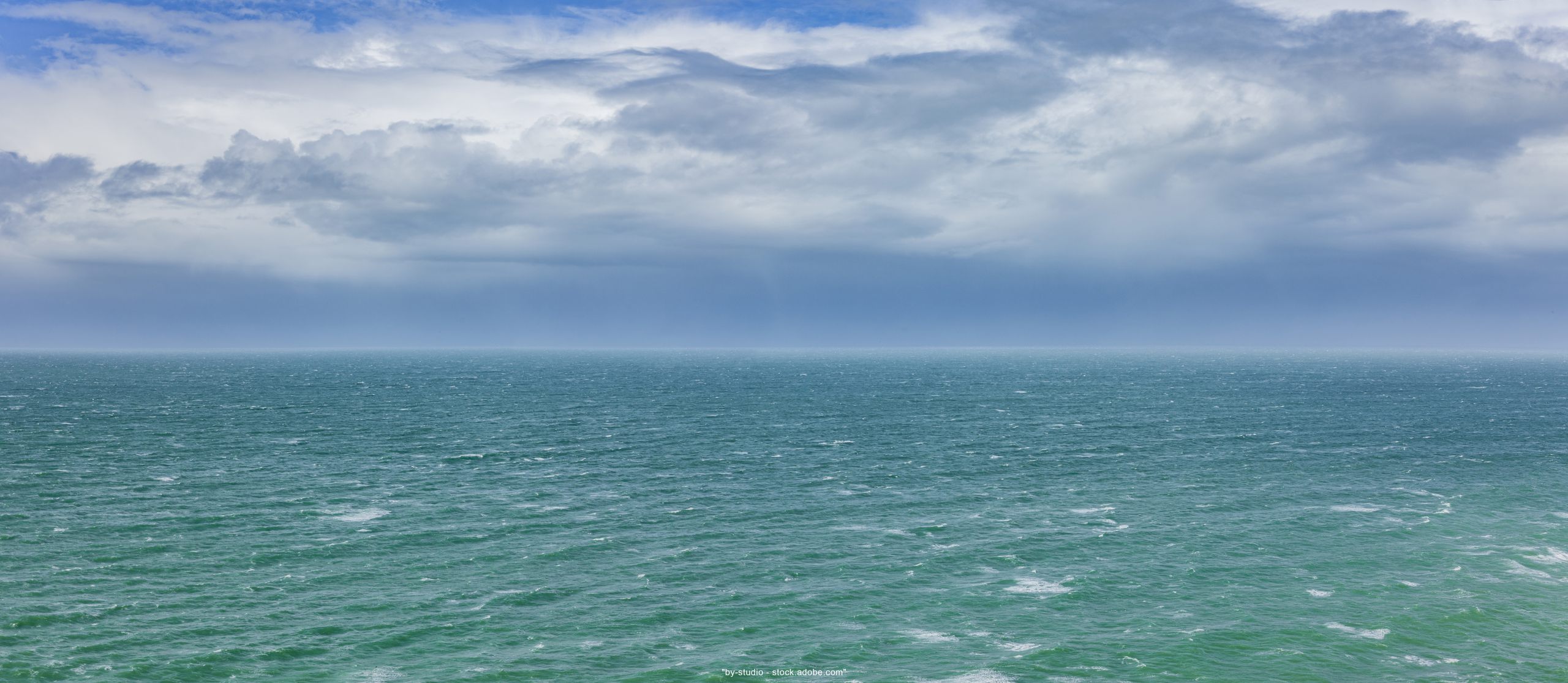 Foto unten türkises Meer mit leichten Wellen oben hellblauer Himmel mit weißen Wolken