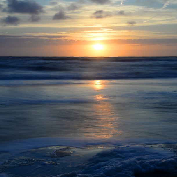 Foto vorne tief dunkel blaues Meer und darüber die dunkel gelbe Sonne welche am Horziont im Meer versinkt